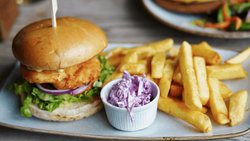 Crispy fried chicken sandwich with lettuce and purple onion on a bun, served with golden fries and purple cabbage slaw.