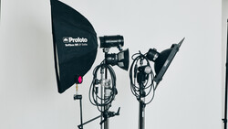 Three professional studio lighting fixtures mounted on stands against a white backdrop.