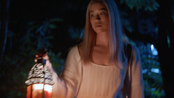 Woman holding illuminated lantern outdoors at night with cool blue ambient lighting.
