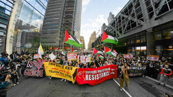 Large protest march filling a city street with Palestinian flags and demonstrators holding signs.