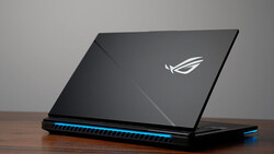 Gaming laptop with illuminated blue accents and winged logo on dark lid, photographed at an angle on wooden surface.