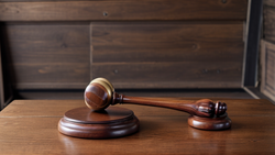 Wooden gavel and sound block arranged on a polished wood desk against a dark wooden background.