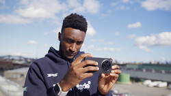 Photographer holding a compact camera while looking at the LCD screen in outdoor daylight.