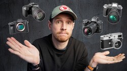 Photographer wearing cap with hands gesturing uncertainty, surrounded by six different camera models floating around him.