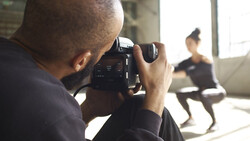 Cinematographer filming a subject indoors using a professional video camera.