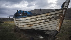 Weathered wooden fishing boat beached on barren grassland with mountains in background.