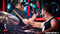 Drummer performing at an indoor venue with stage lighting and drum kit visible.