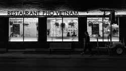 Black and white storefront of a Vietnamese pho restaurant with three large display windows and illuminated signage at night.