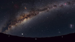 The Milky Way galaxy stretches diagonally across a starry night sky above a dark silhouetted landscape.