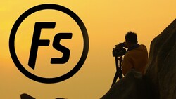 Silhouetted photographer operating a camera on a rocky outcrop against a golden yellow sky with the Fstoppers logo.