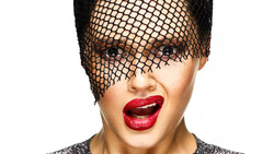 Person wearing black mesh headpiece with bold red lipstick and neutral eye makeup against white background.