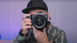 Photographer holding a Fujifilm medium format camera up to eye level, wearing a black baseball cap and plaid shirt.