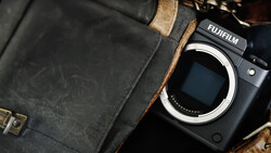 Fujifilm mirrorless camera body next to vintage leather camera bag with brass hardware.