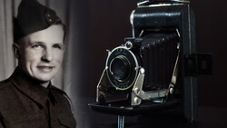 Man in military uniform posing beside a large format folding camera on a stand.
