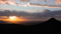Silhouetted volcanic cone against a golden sunset with dramatic cloud formations and warm orange light breaking through the sky.