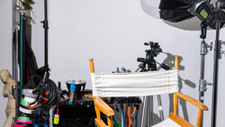 Photography studio setup with lighting equipment, reflectors, and production gear arranged on tables.