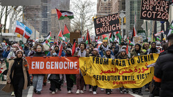 Large crowd of protesters holding banners and flags during an outdoor march in an urban setting.