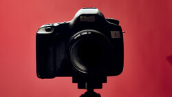 Canon DSLR camera with telephoto lens mounted on tripod against red backdrop.