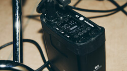 Black audio recorder with control panel and microphone attachment on beige surface with cables.