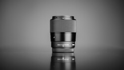 Sony mirrorless camera lens with silver and black barrel standing upright against neutral background.
