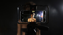 Smartphone mounted on a gimbal displaying a portrait of a shirtless man in a dark studio setting.