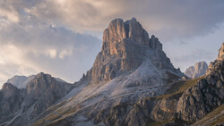Dramatic alpine peak with steep columnar rock formations and early snow in golden hour light.