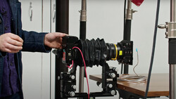 Photographer adjusting a lens on a cinema camera mounted to a wooden support rail.