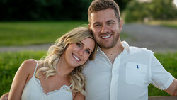 Couple posing together outdoors on a lawn, smiling at camera in natural daylight.