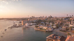 Coastal waterfront neighborhood at golden hour with bay, docks, and distant skyline under clear sky.