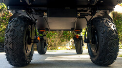 Undercarriage view of an all-terrain vehicle with large knobby black tires and yellow suspension components.