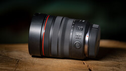 Telephoto zoom lens with red accent ring positioned on wooden surface against dark background.