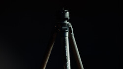 Tripod head mounted on pole against dark background with dramatic sidelighting.