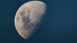 Waxing gibbous moon against dark blue sky showing craters and dark maria in sharp detail.