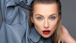 Woman with bold red lipstick wearing a blue-gray jacket against neutral background.