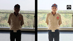 Two men in tan uniforms with red patches standing indoors with forested landscape visible through windows behind them.