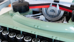Close-up of a vintage typewriter with mint green body and black keys, showing mechanical components and ribbon mechanism inside.