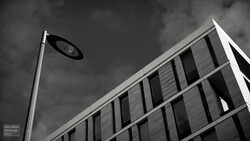 Street lamp against dramatic cloudy sky with modernist building facade featuring vertical window lines.