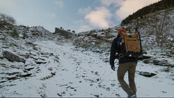 Backpacker hiking across snowy alpine terrain with yellow and brown pack on their back.