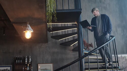 Man on industrial metal staircase reading a document while warm pendant light glows nearby.