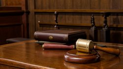 Judge's gavel and law books arranged on a wooden desk in a courtroom setting.