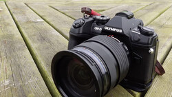 Olympus OM-D mirrorless camera with attached zoom lens on wooden deck surface.