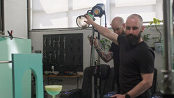Two photographers adjusting a studio light on a stand during a production setup.