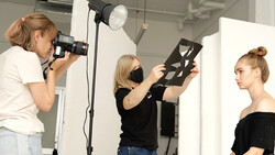 Three photographers working on a studio portrait shoot with professional lighting setup and reflector.