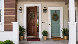 Symmetrical front porch with two painted doors, coordinating wreaths, potted plants, and wall sconces flanking a central chimney.