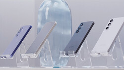 Five smartphones in different colors displayed at angles on clear acrylic stands with a translucent blue bottle in the center background.