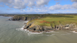 Coastal headland with steep green cliffs dropping to rocky shoreline and churning surf below.