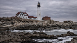 White lighthouse with red-roofed keeper's house on rocky Maine coast during overcast conditions.