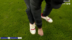 Overhead view of a player's feet in white and red sneakers on a grass pitch during a live soccer match.