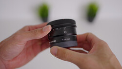 Hands holding a wide-angle camera lens with manual focus ring and aperture markings visible.