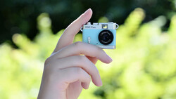 Hand holding a light blue vintage compact camera against a blurred green foliage background.
